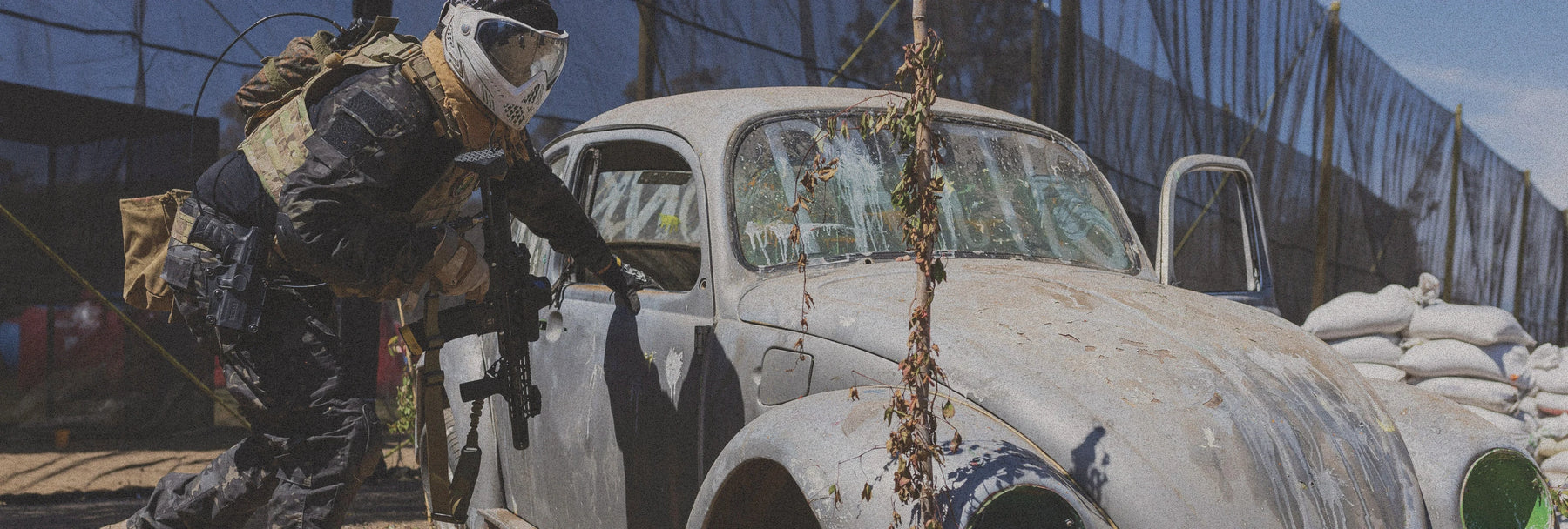 Person in military gear interacting with a vintage car in a desert setting