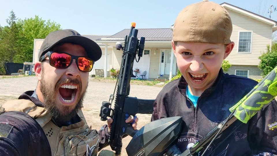 Nightmare PB posing with his son, holding an EMF200 magfed paintball marker, both smiling in paintball gear.